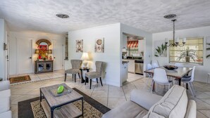 A spacious living area with a sofa, chairs, a coffee table, and a dining table with chairs. There is a kitchen area with a sink and stove, and a dining area with a chandelier. - Quiet North End Home Only 2 Blocks to Beach with Private Pool (Anna Maria)