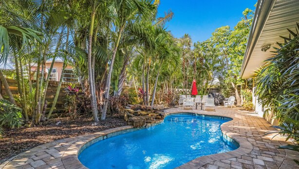A swimming pool with a brick border, surrounded by palm trees and a patio area with outdoor furniture. - Quiet North End Home Only 2 Blocks to Beach with Private Pool (Anna Maria)