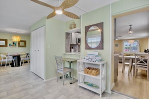 A room with a ceiling fan, a dining area with a table and chairs, a white cabinet, and a shelf with baskets. - Remodeled Duplex with Heated Pool, 2 Blocks to the Beach! (Anna Maria)