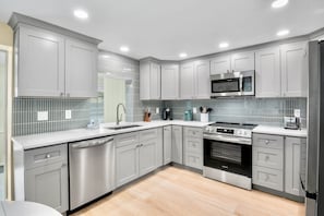 A modern kitchen with grey cabinetry, stainless steel appliances, and a tiled backsplash. - Remodeled Duplex with Heated Pool, 2 Blocks to the Beach! (Anna Maria)