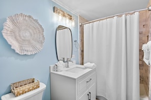 Un baño con un lavamanos blanco, un espejo, una cortina de ducha y un adorno en la pared.