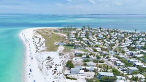 Vista aérea de un complejo turístico en la costa, con playa, casas y aguas azul turquesa.