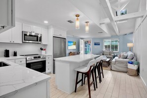 A modern kitchen with white cabinetry, a central island, and a dining area with a grey sofa and bar stools.