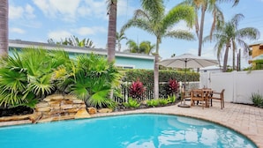 A swimming pool with a stone waterfall, surrounded by tropical plants and a patio with outdoor furniture. - Duplex with Heated Pool! 2 Blocks to Beach! - Turtle Crawl (Anna Maria)