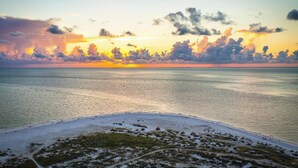Een strand met een helder uitzicht op de oceaan en een ondergaande zon op de achtergrond.