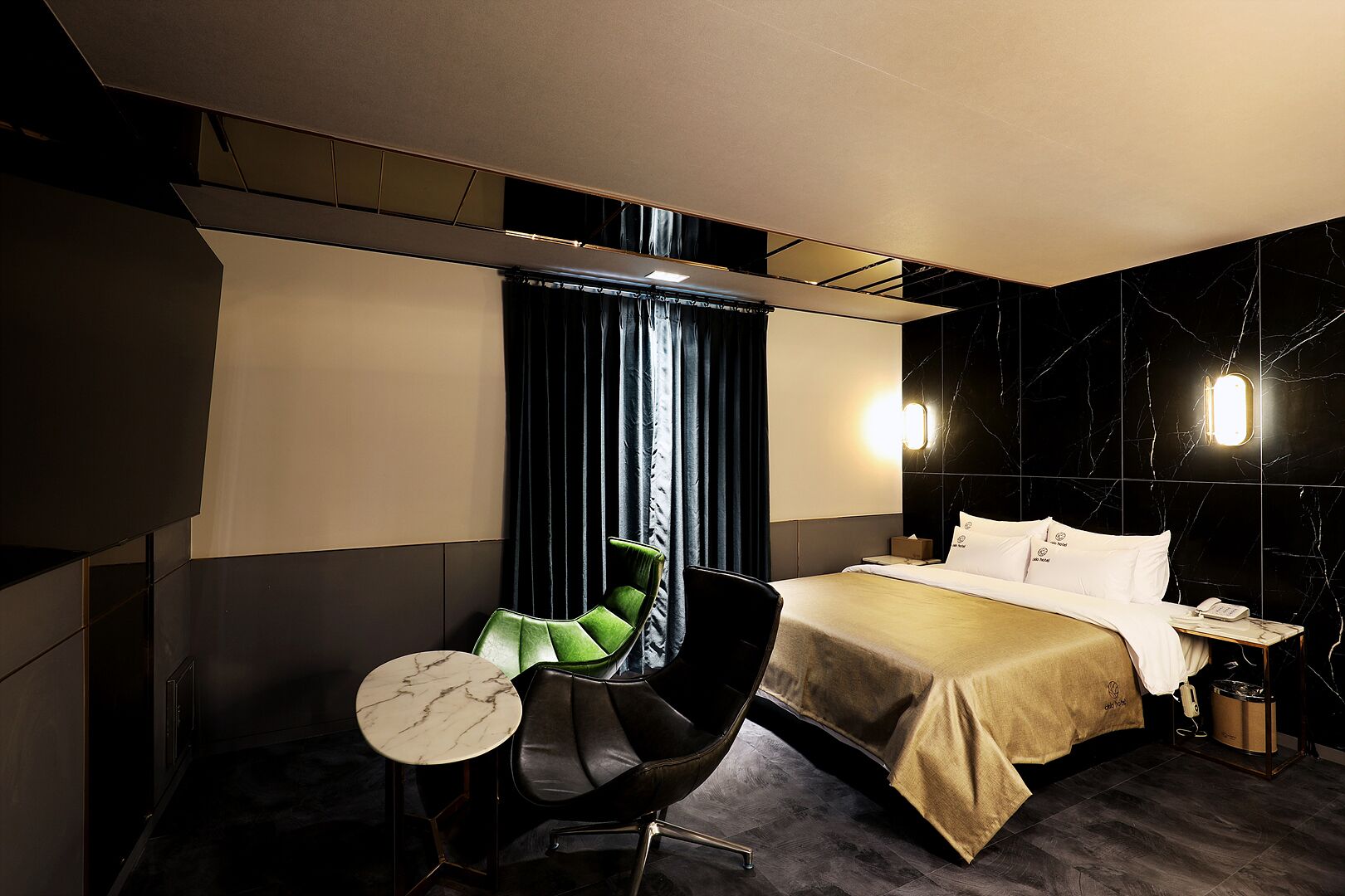A modern hotel room with a bed, a green chair, a small round table, and a nightstand with a lamp.