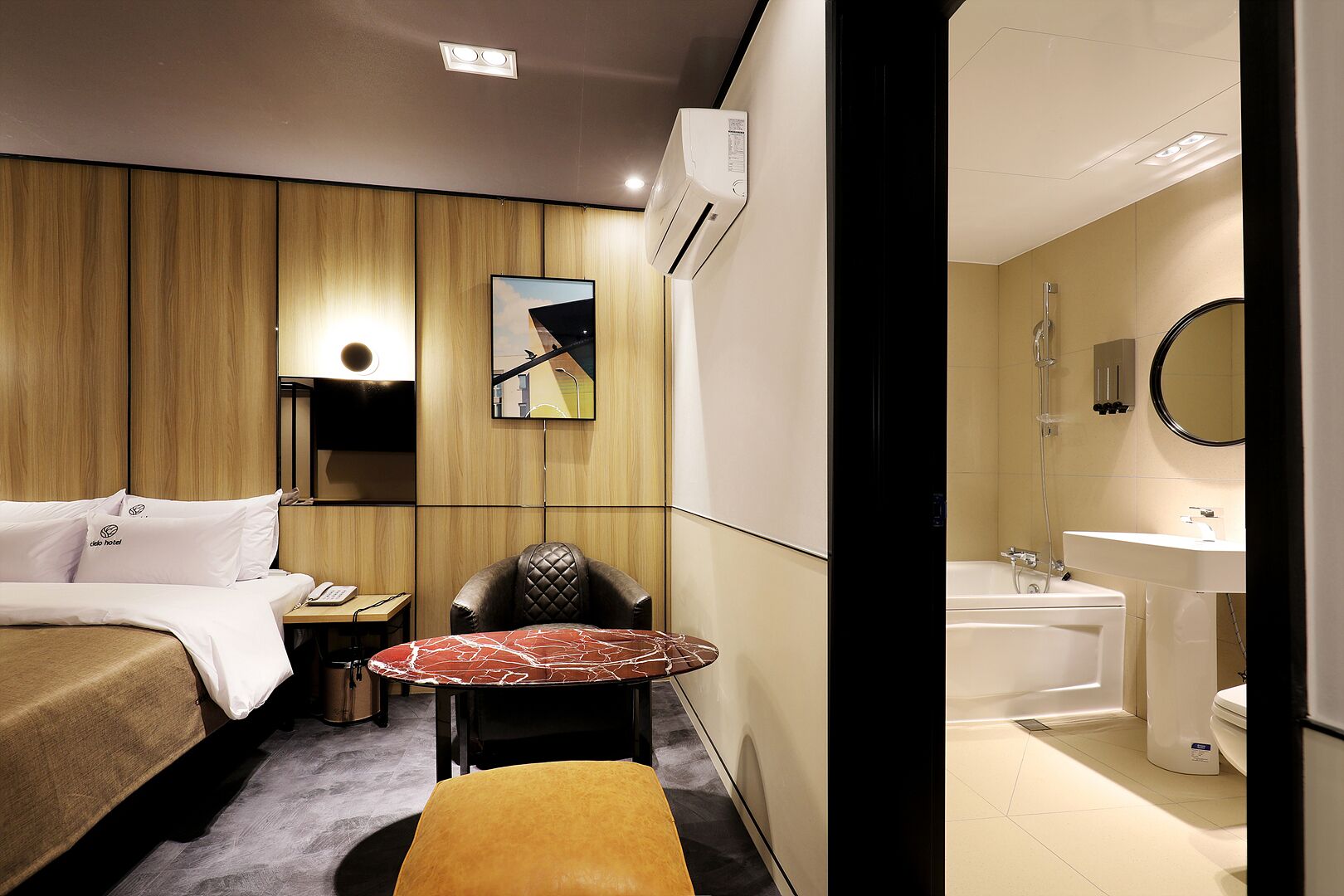 Quarto de hotel com cama, escrivaninha, cadeira, mesa pequena, banheiro com banheira e espelho.