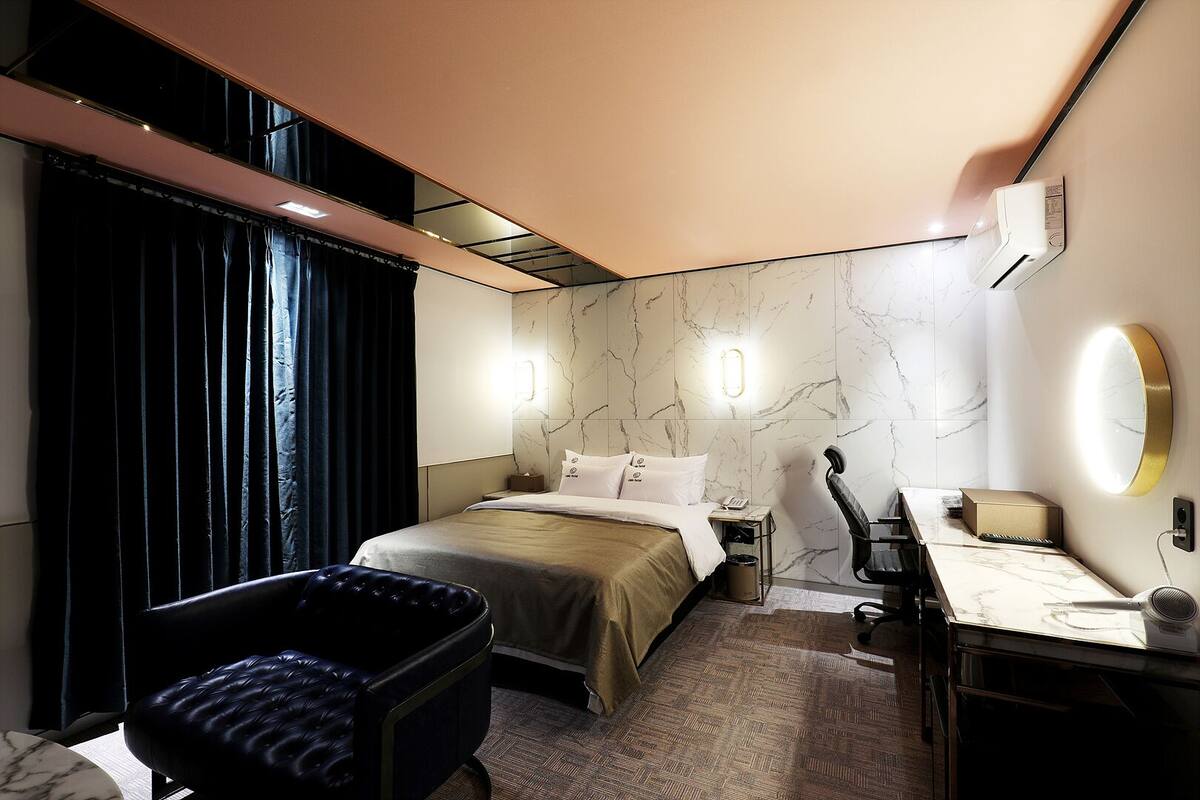 A modern hotel room with a bed, a desk, a chair, and a large window with curtains.
