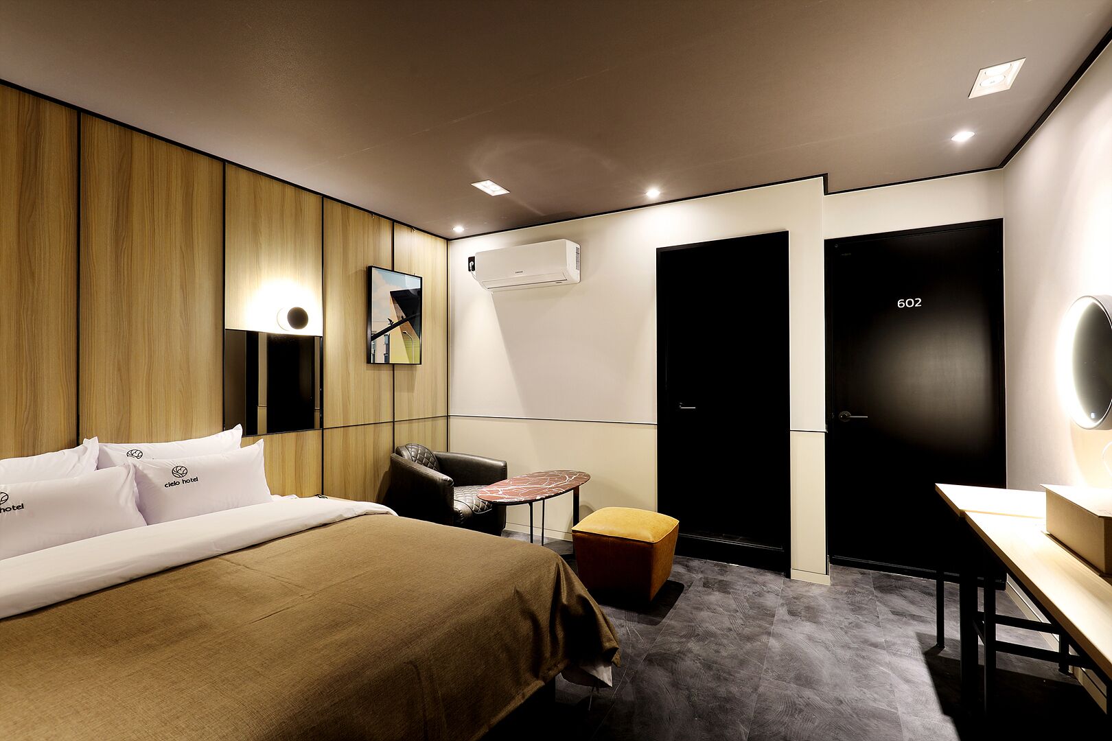 A hotel room with a bed, a desk, a chair, a small table, and a mirror.
