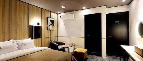 A hotel room with a bed, a desk, a chair, a small table, and a mirror.