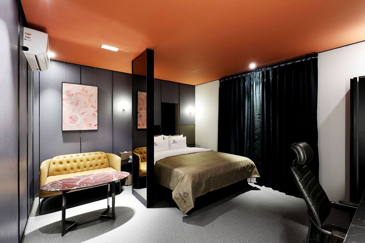 A modern hotel room with a bed, a sofa, a desk, and a chair.