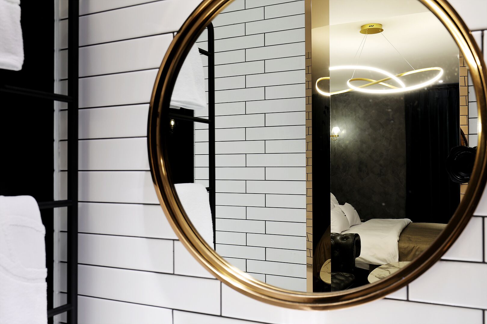 A modern bathroom with a large oval mirror, white tiled walls, and a black towel rack.