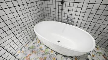 A bathroom with a white bathtub, a shower, and a tiled floor with floral patterns.