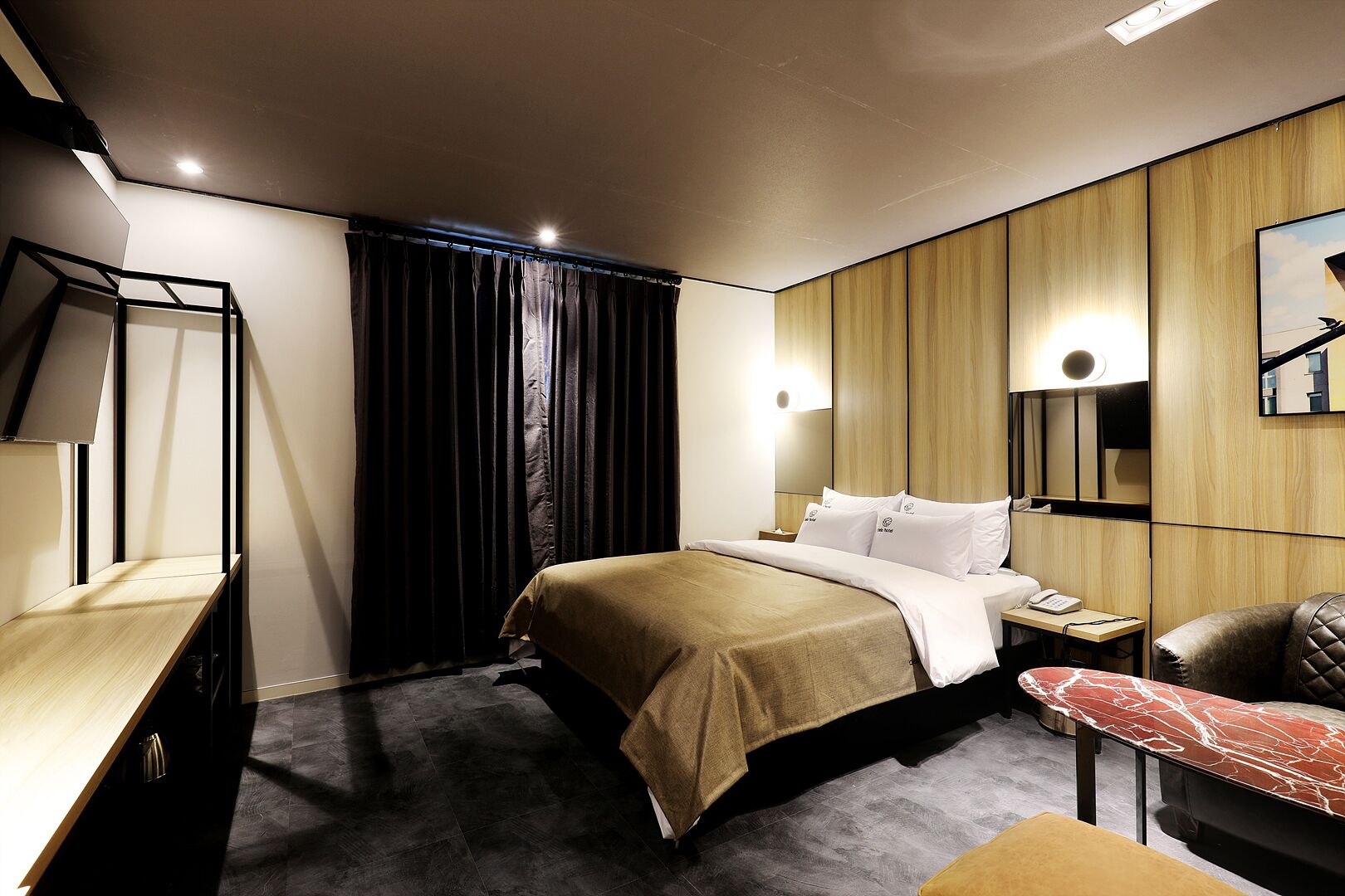 A modern hotel room with a bed, bedside table, chair, and a large mirror.