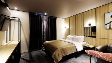 A modern hotel room with a bed, bedside table, chair, and a large mirror.