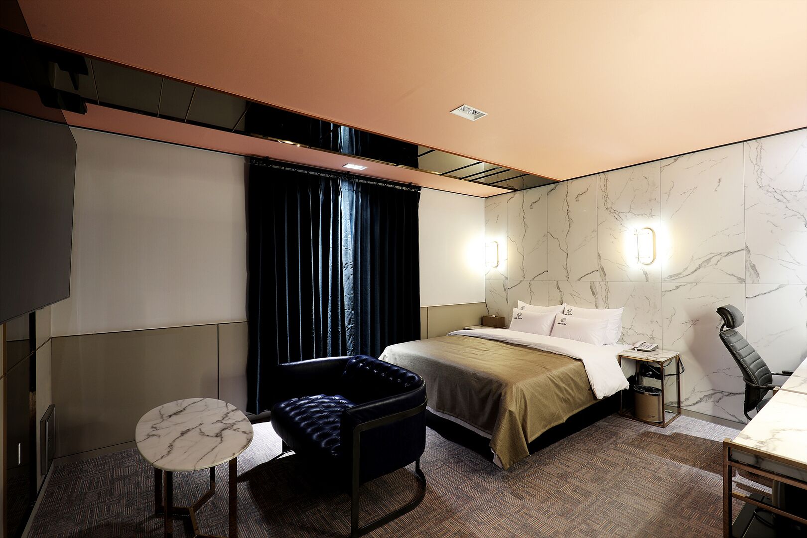 Habitación de hotel con cama, escritorio, silla, una mesita y ventana con cortinas.