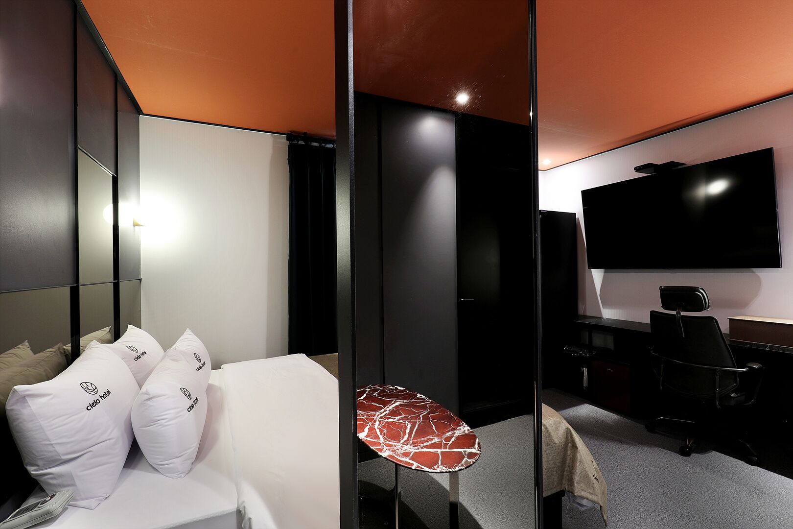 Una habitación de hotel moderna con cama, escritorio, silla, televisor y una mesita.