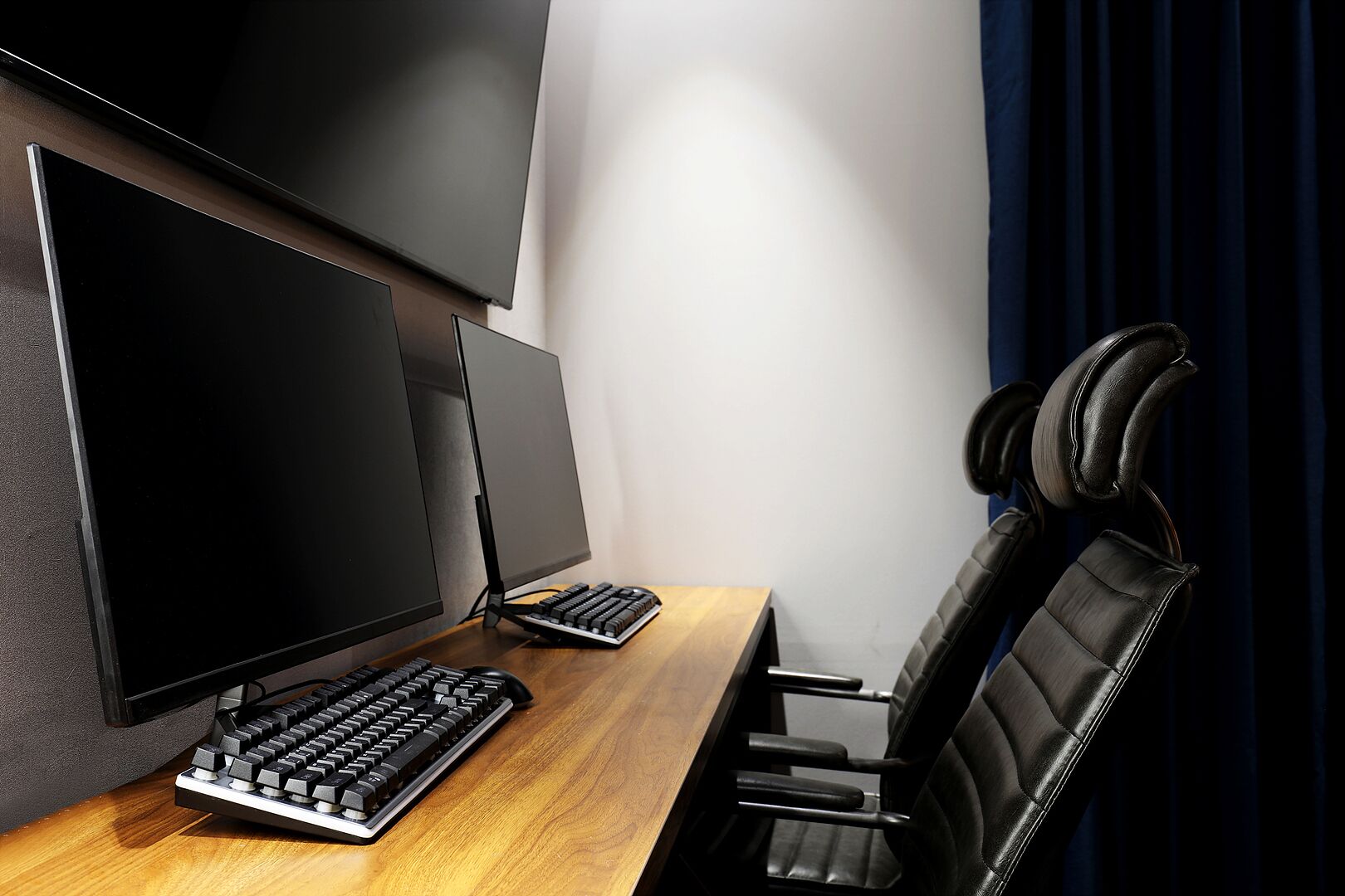 Ein Home-Office-Arbeitsplatz mit einem Holztisch, einer schwarzen Tastatur, einem großen Bildschirm und einem schwarzen Ledersessel mit Kopfhörern.