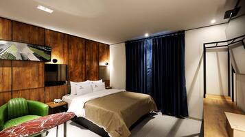 A modern hotel room with a bed, a green chair, a small table, and a TV mounted on the wall.