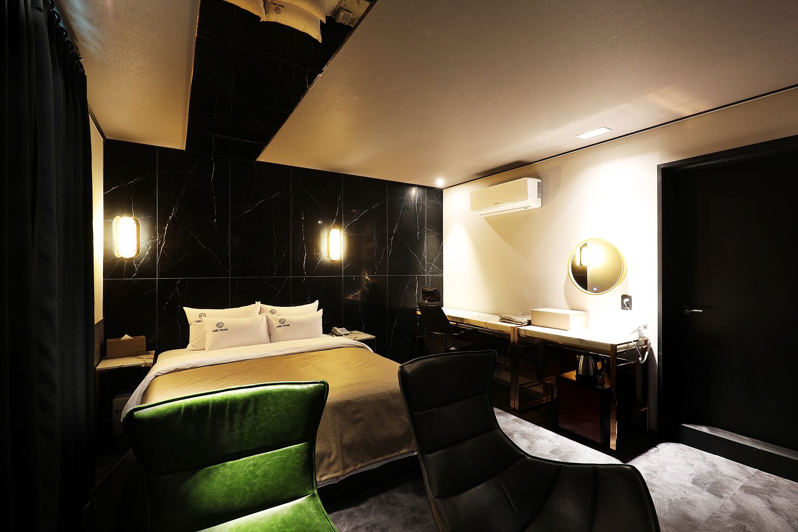 A hotel room with a bed, a desk with a mirror, a chair, and a vanity with a sink.