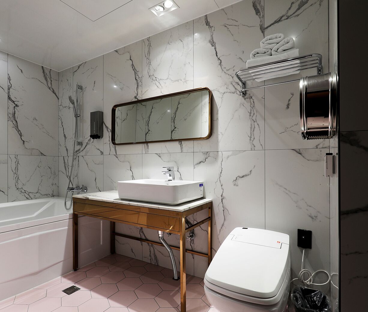 A modern bathroom with a marble wall, a sink, a mirror, a towel rack, a toilet, and a shower.