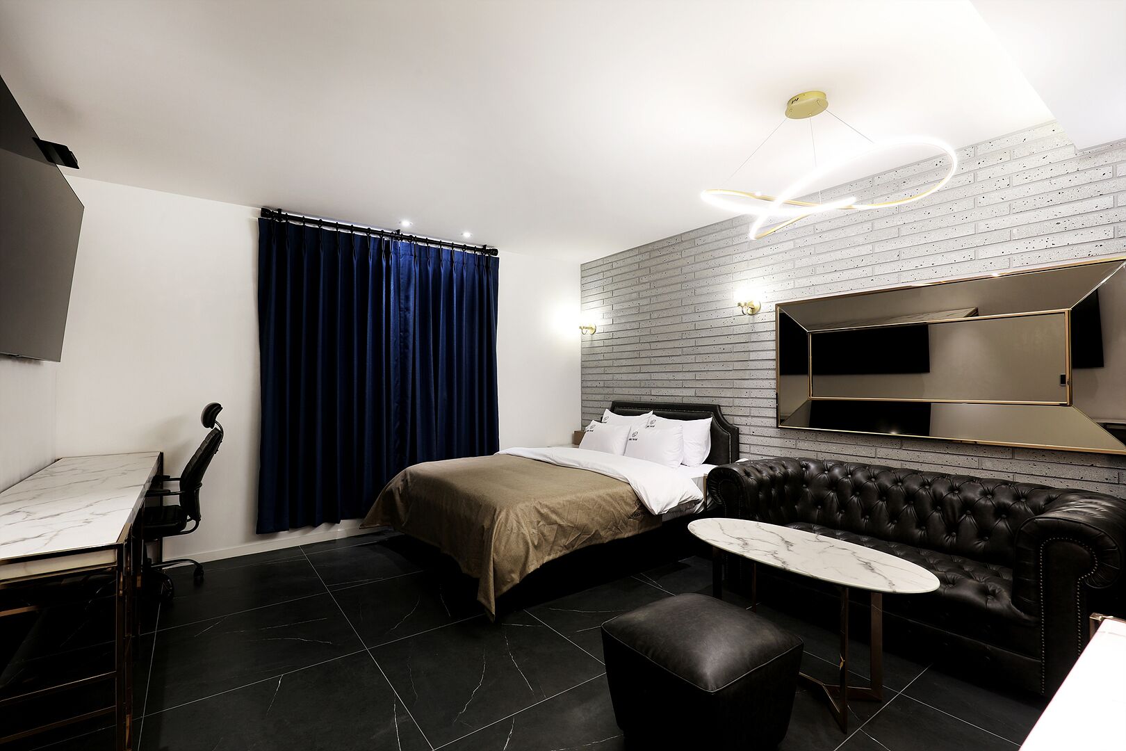 A modern hotel room with a bed, a leather sofa, a small table, and a TV mounted on the wall.