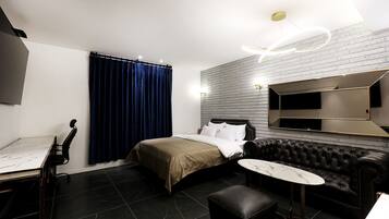 A modern hotel room with a bed, a leather sofa, a small table, and a TV mounted on the wall.