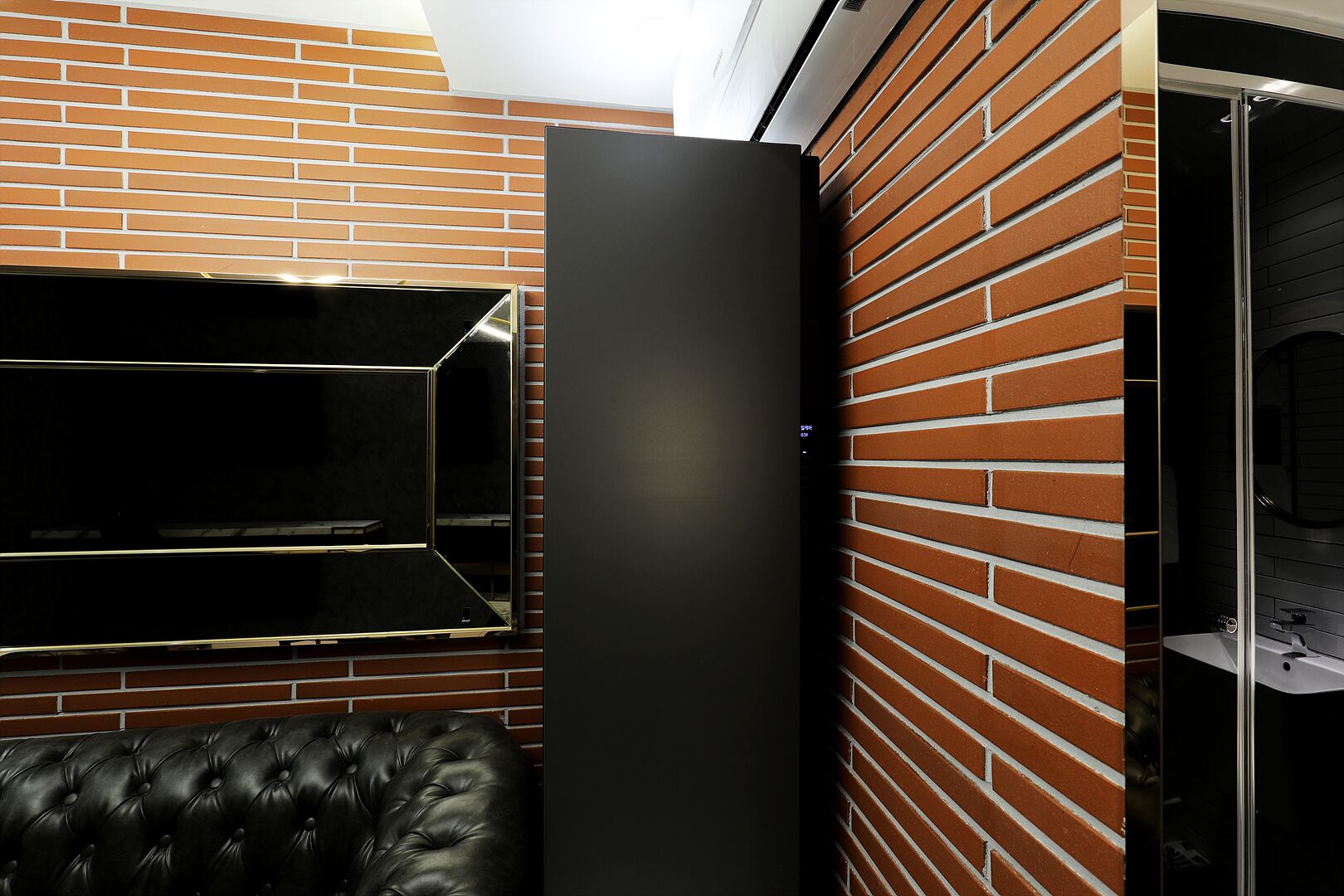 A modern room with a brick wall, a black leather sofa, and a black cabinet.