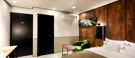 Una habitación de hotel moderna con una cama, una silla verde, una mesita y un televisor en la pared.