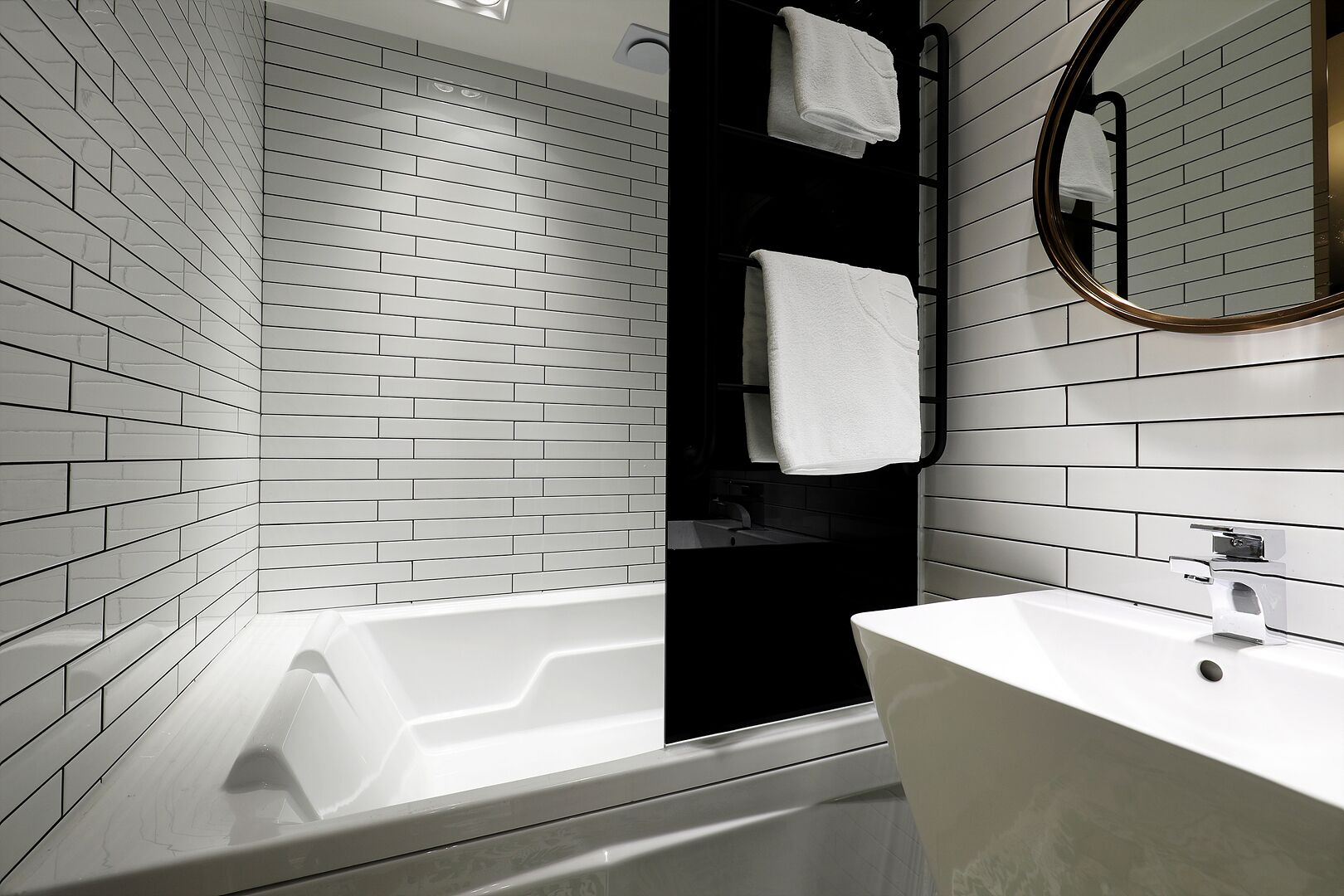Un baño moderno con azulejos blancos tipo metro, una bañera, un lavabo y un espejo.