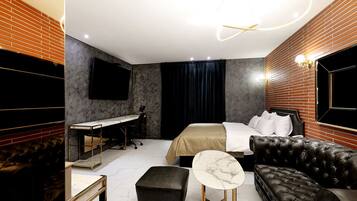 Una habitación de hotel moderna con una cama grande, un escritorio, un sofá de cuero y una mesita redonda.