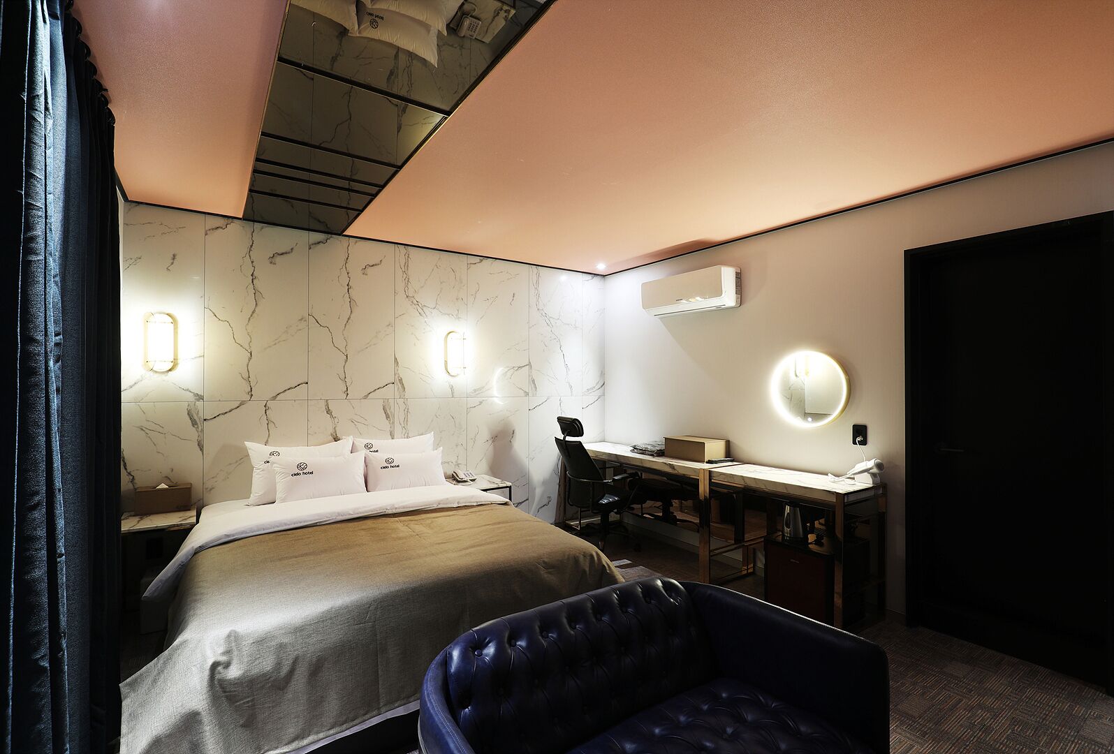 A modern hotel room with a bed, a desk, a chair, and a large mirror.
