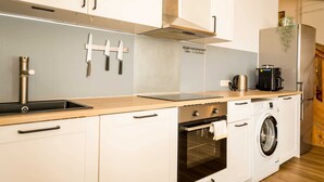 A modern kitchen with white cabinets, a stainless steel range hood, a built-in oven, a washing machine, and a coffee maker. - Spacious 3 Bedroom Apartment Online Check-In (Berlin)