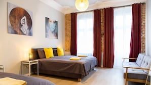 Een slaapkamer met een groot bed, een kleiner bed, een slaapbank en een nachtkastje met een lamp.