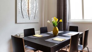En spisestue med et sort bord, seks stole, en vase med blomster og et fjer-kunstværk på væggen.