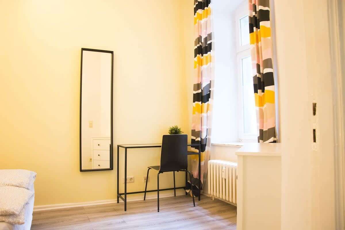 Um quarto pequeno e luminoso com uma cadeira preta, uma mesinha e um radiador.