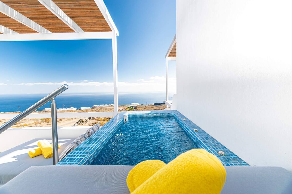 A small outdoor hot tub with a view of the sea, a wooden ceiling, and a white wall.