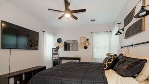 Ein Schlafzimmer mit Bett, Deckenventilator, Fernseher, Kommode und Wanddekoration.