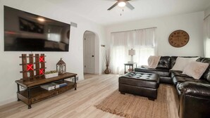 Ein Wohnzimmer mit Flachbildfernseher, Deckenventilator, Uhr, Sofa und Couchtisch.