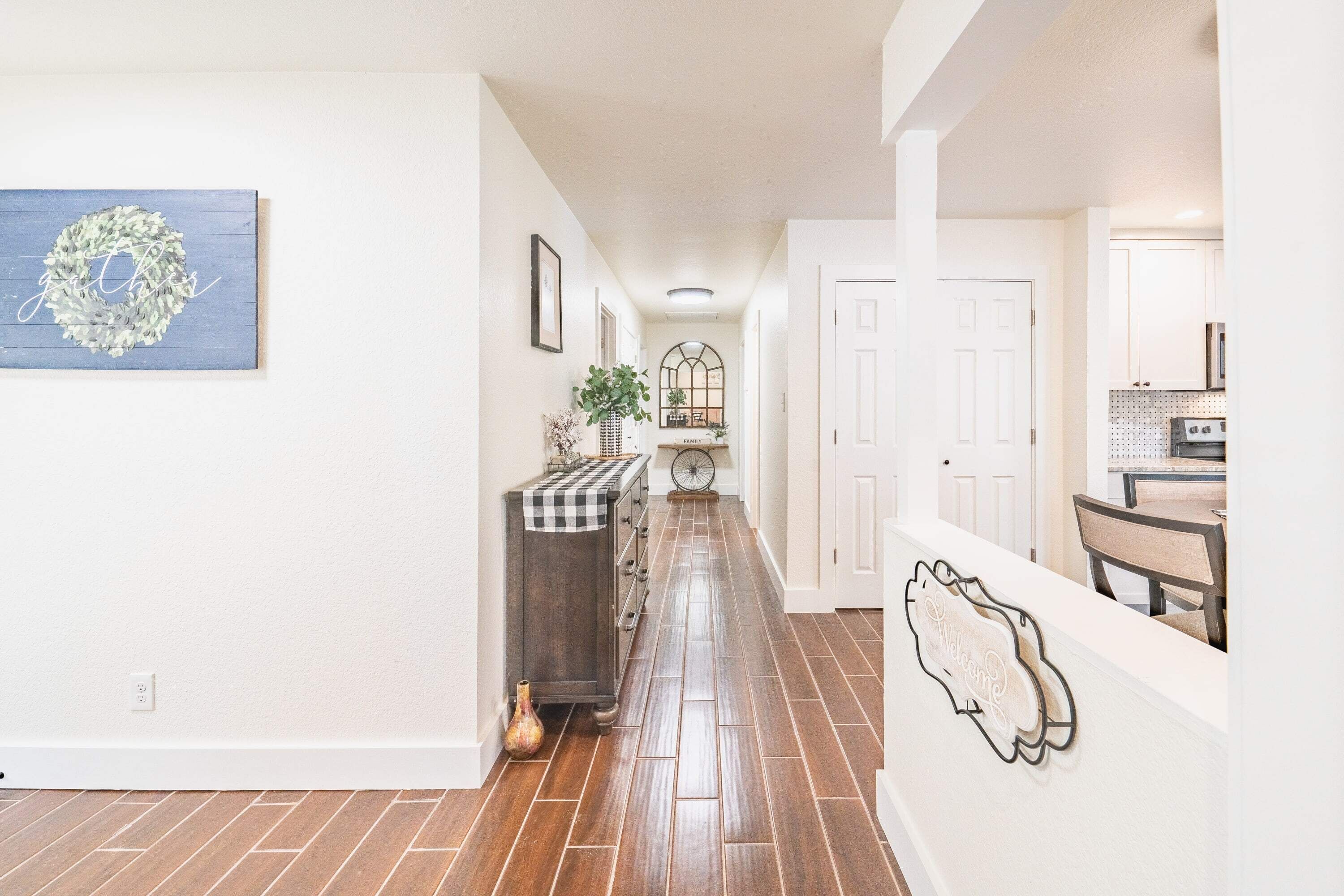 Un couloir avec un plancher en bois, une guirlande décorative, un tissu à carreaux sur un meuble et une pancarte de bienvenue accrochée au mur.