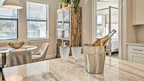 Un comedor con una mesa de mármol, dos copas de cristal, una botella de champán y un aparador con plantas.