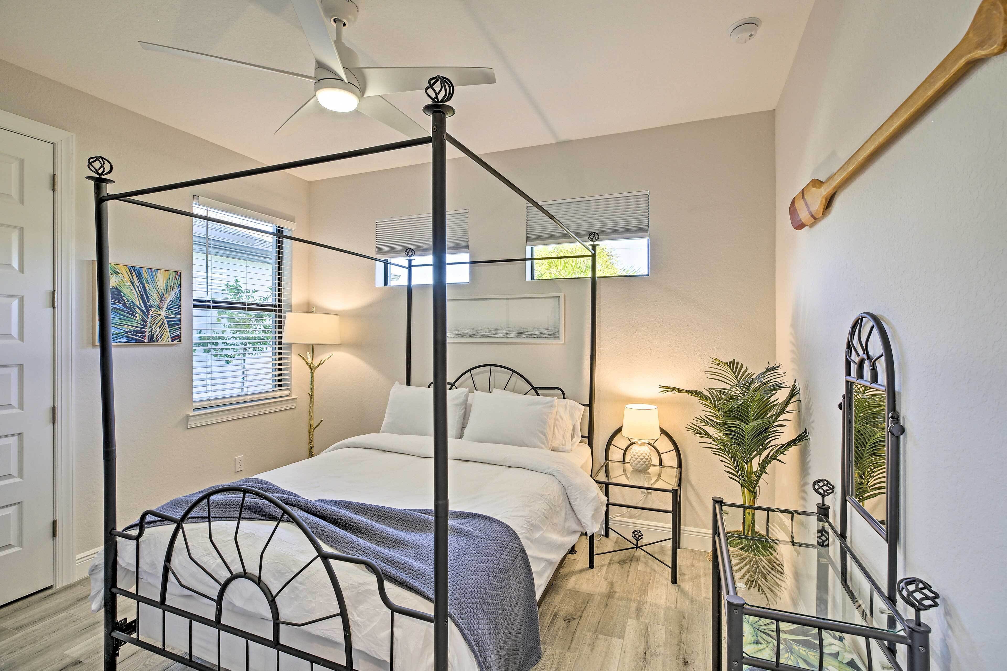 Ein Himmelsbett mit Deckenventilator, ein Nachttisch mit Lampe, ein Blumentopf und ein Spiegel an der Wand.