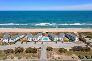 A beachfront hotel with multiple buildings, a central pool, and a view of the ocean.