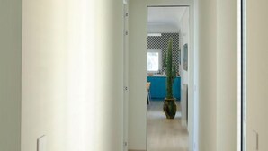 A hallway with a wooden floor leading to a room with a blue accent wall and a potted plant.