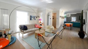 A spacious living area with a sofa, chairs, a dining table, and a kitchen in the background.
