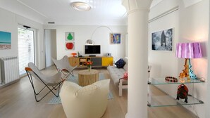 A modern living room with a sofa, chairs, a TV, and a glass coffee table.