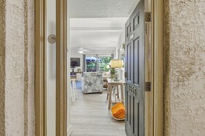 Un pasillo que conduce a un comedor con ventilador de techo, televisor y vistas al exterior.