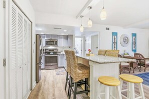 Une cuisine équipée d’un four à micro-ondes, d’un four et d’un réfrigérateur, un coin bar avec des tabourets, des chaises en osier et une table à manger avec des chaises.