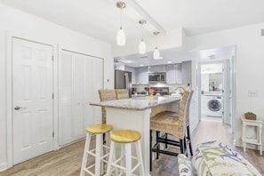 Une cuisine compacte dotée d’un îlot central, de tabourets de bar, d’un lave-linge et d’un espace dédié à la buanderie.