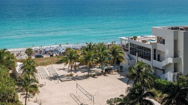 Un hôtel situé en bord de mer, doté d’une piscine, de palmiers et offrant une vue sur l’océan.